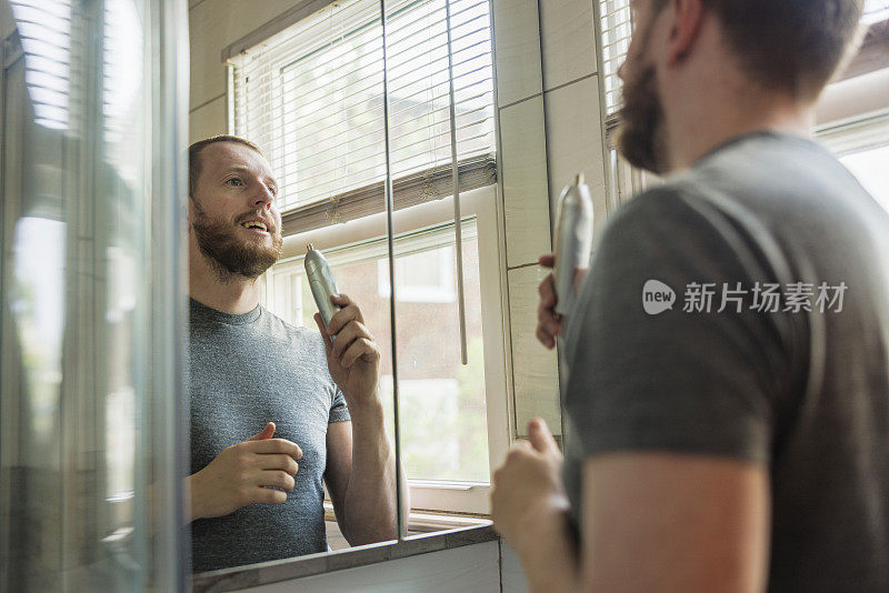 一名白种白人男子在一间现代化的浴室里使用一种带耳朵/鼻孔脱毛附件的便携式无线修剪器。